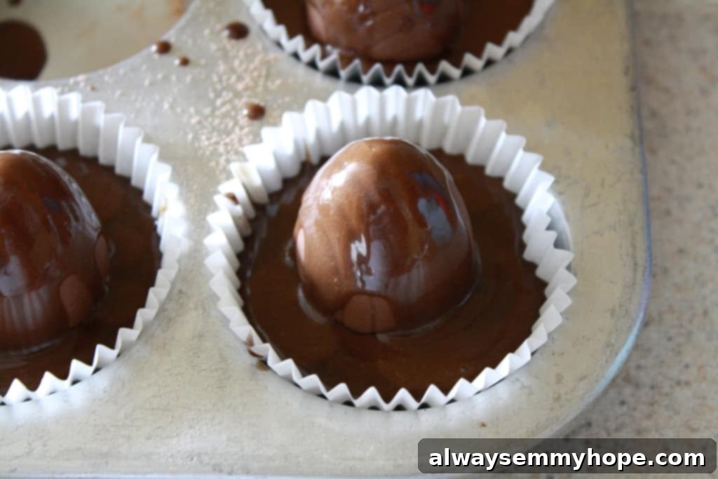 A whole Cadbury chocolate egg being placed into a cupcake liner filled with chocolate batter, ready for baking. The surprise is perfectly nestled.