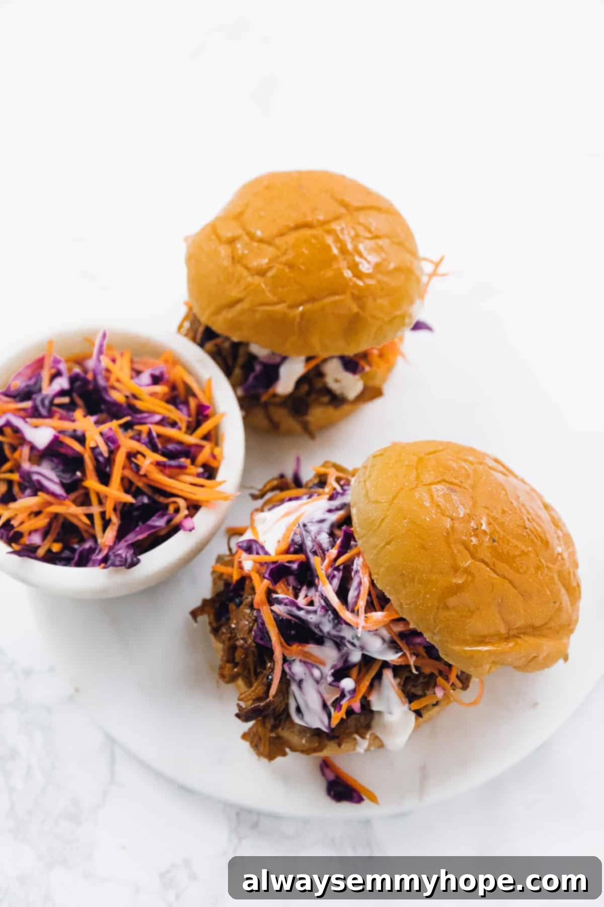 Smoky Vegan Pulled Mushroom Sandwiches 4 Top down view of two vegan pulled mushroom sandwiches on a white plate with a bowl of slaw on the side.