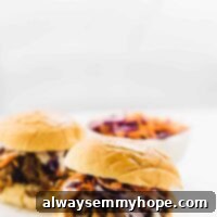 Smoky Vegan Pulled Mushroom Sandwiches 7 Side on shot of two vegan pulled pork sandwiches on a white plate, with slaw in the background.