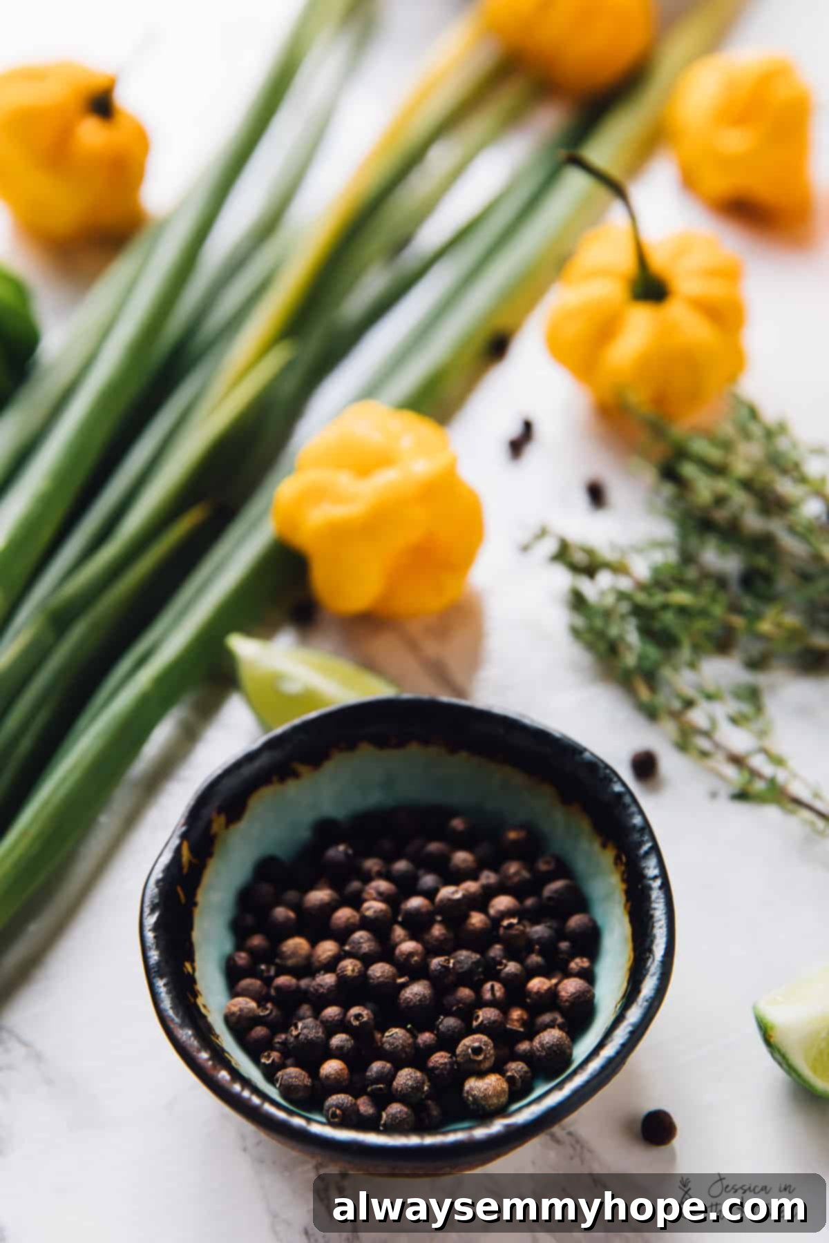 Easy Homemade Jamaican Jerk Sauce 6 Close-up of pimento seeds in a small bowl, with scotch bonnet peppers blurring in the background.