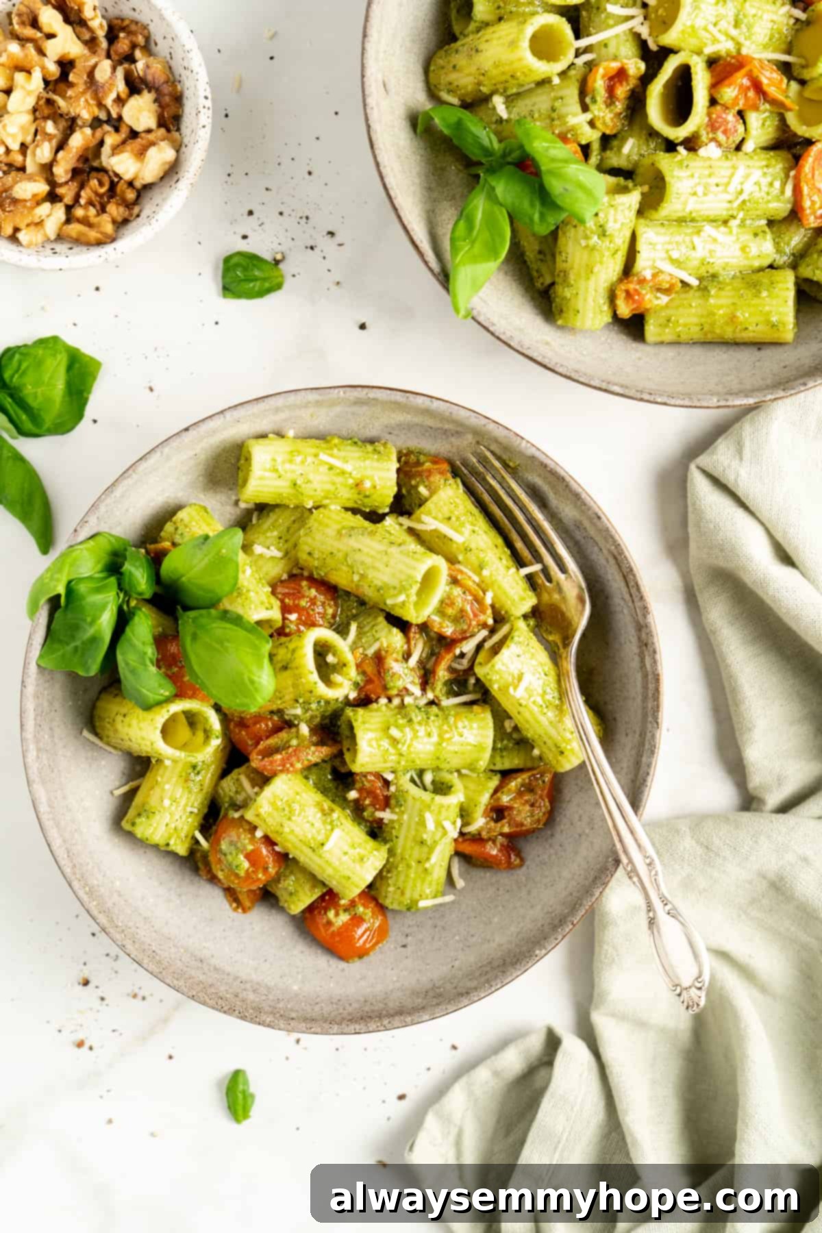 Overhead view of two bowls filled with pasta, pesto, cherry tomatoes, basil, and vegan parmesan cheese