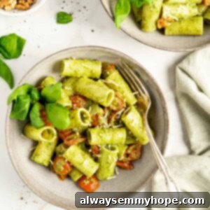 Overhead view of two bowls filled with pasta, pesto, cherry tomatoes, basil, and vegan parmesan cheese