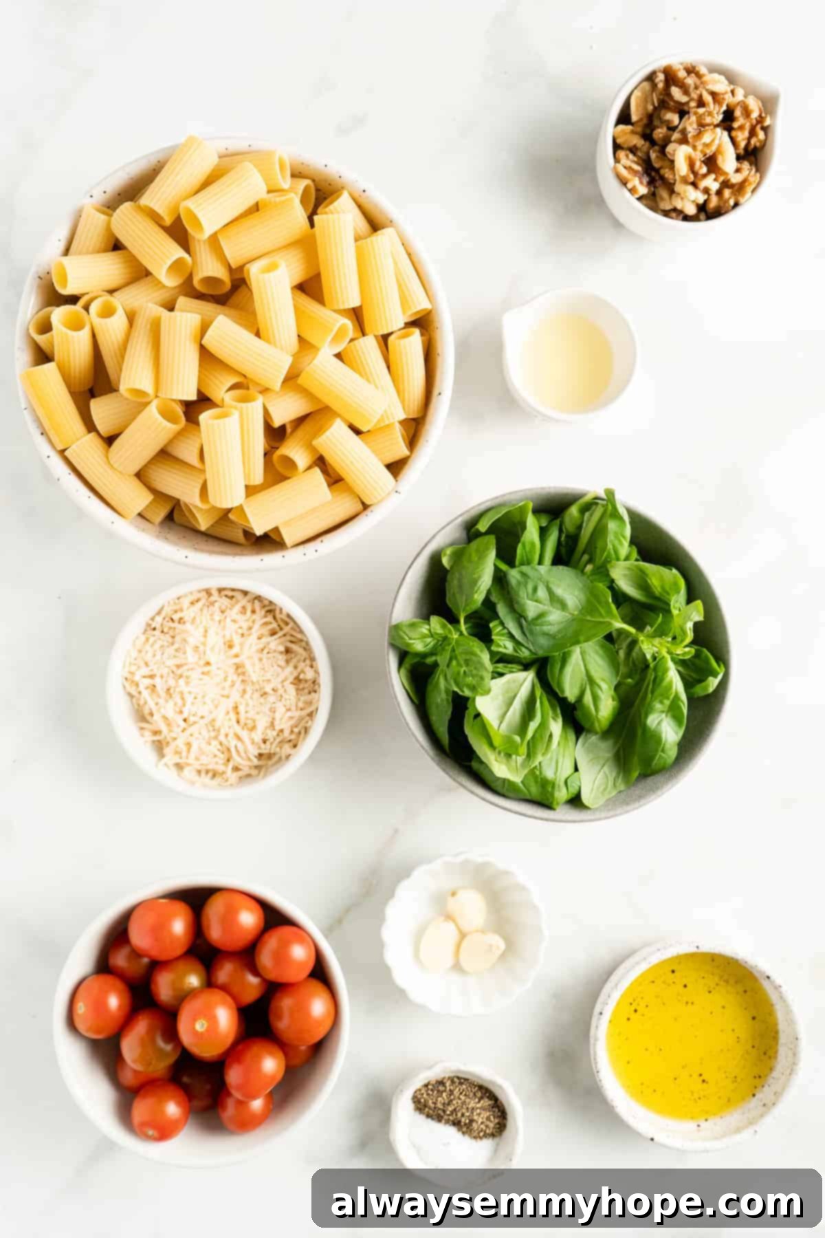 Overhead view of ingredients for pesto pasta including fresh basil, walnuts, garlic, olive oil, and cherry tomatoes