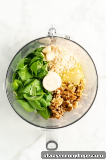 Overhead view of basil, garlic, walnuts, oil and vegan parmesan cheese sitting inside of a food processor with the lid off