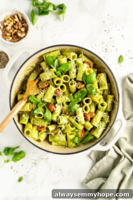 Overhead view of pesto pasta in bowl with wooden spatula and small bowl of nuts