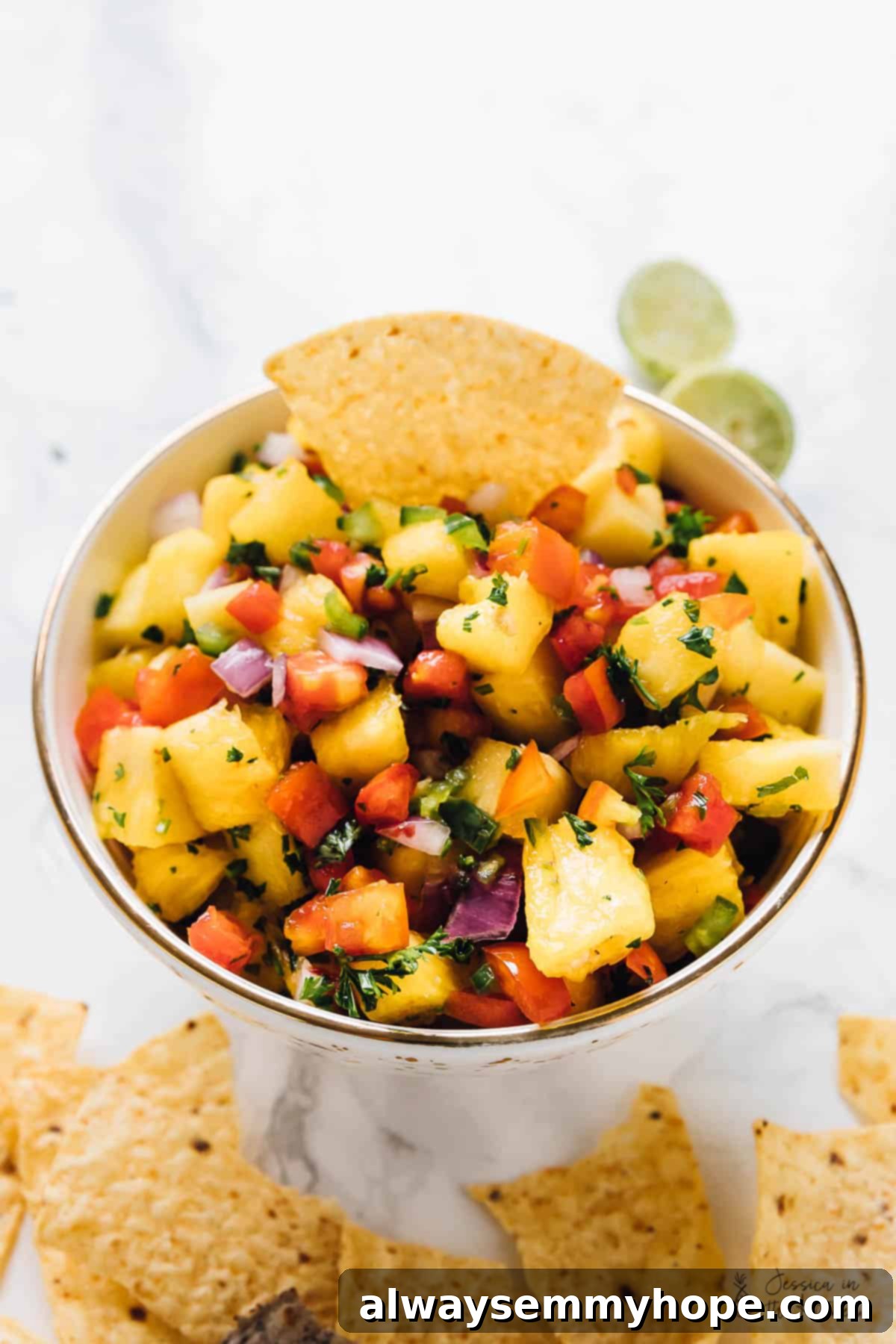 This fresh pineapple salsa recipe with jalapeño, parsley, tomatoes, and onions is the perfect sweet-and-tangy condiment for taco night. Bowl of fresh pineapple salsa recipe with a corn chip, showcasing vibrant colors.