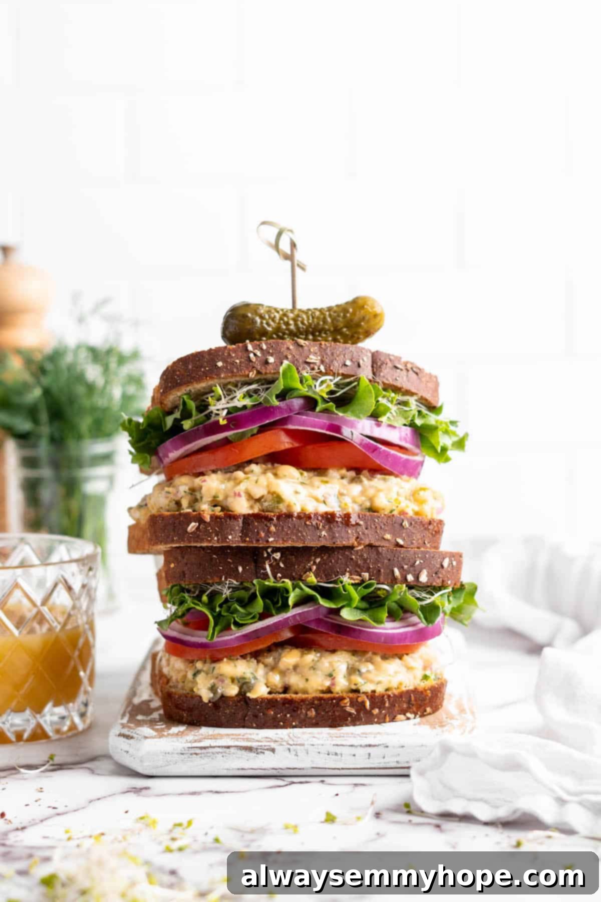 Creamy Vegan Chickpea Tuna Salad 7 Two stacked vegan tuna sandwiches topped with sprouts, lettuce, red onion, and tomatoes
