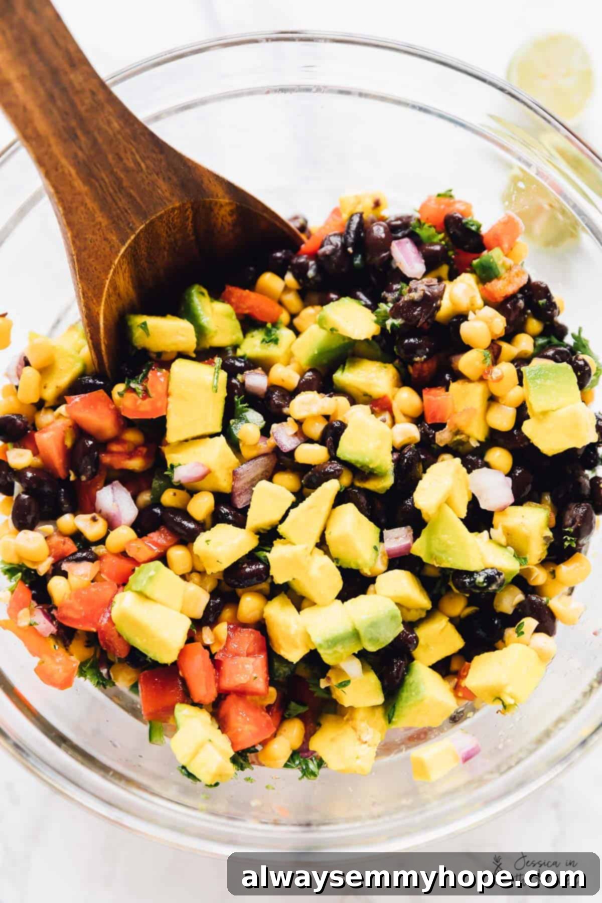 This black bean and corn salsa recipe with creamy avocado, parsley, red onions, and spicy jalapeños is the perfect appetizer with corn chips. Stirring the ingredients for the black bean and corn salsa with a wooden spoon.