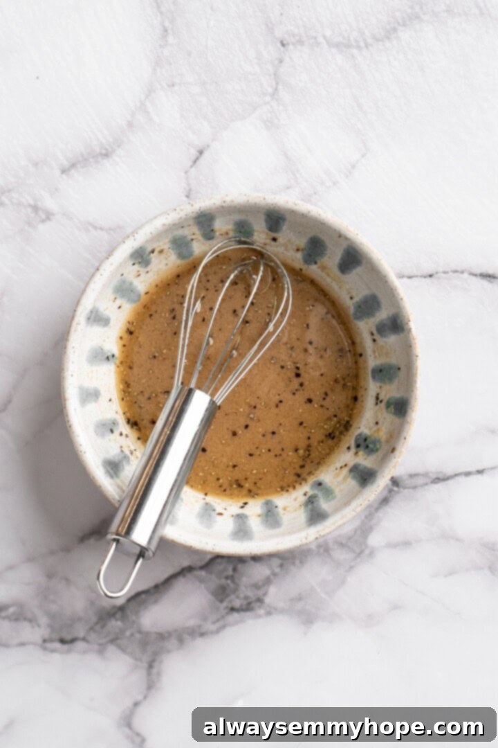 Step 1: Make the vinaigrette. Overhead view of freshly prepared Italian vinaigrette in a small glass bowl with a whisk, ready to be added to the pasta salad.