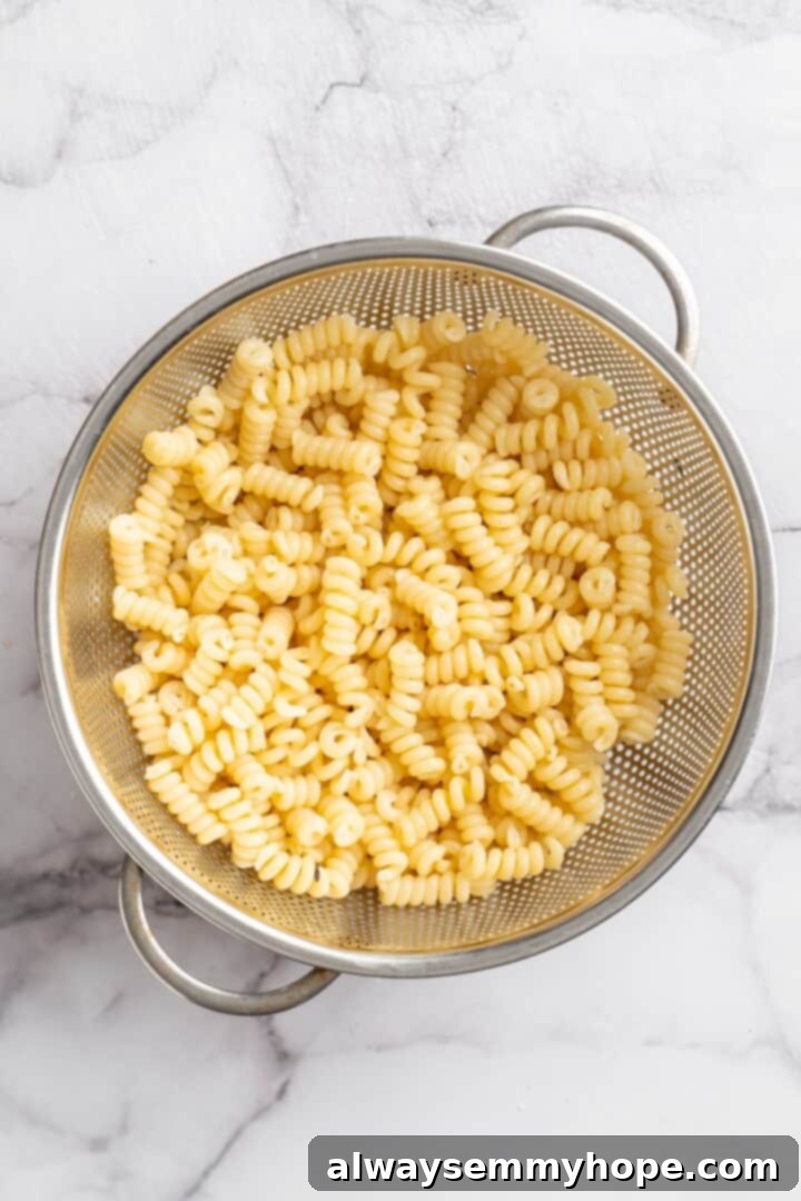 Step 2: Cook the pasta. Overhead view of perfectly cooked rotini pasta draining in a colander, steam gently rising, ready for the pasta salad assembly.