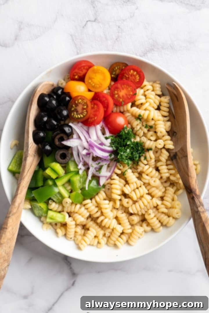 Step 3: Toss to coat. Overhead view of a large mixing bowl filled with cooked pasta, fresh vegetables, and the Italian vinaigrette, being tossed with two wooden spoons.