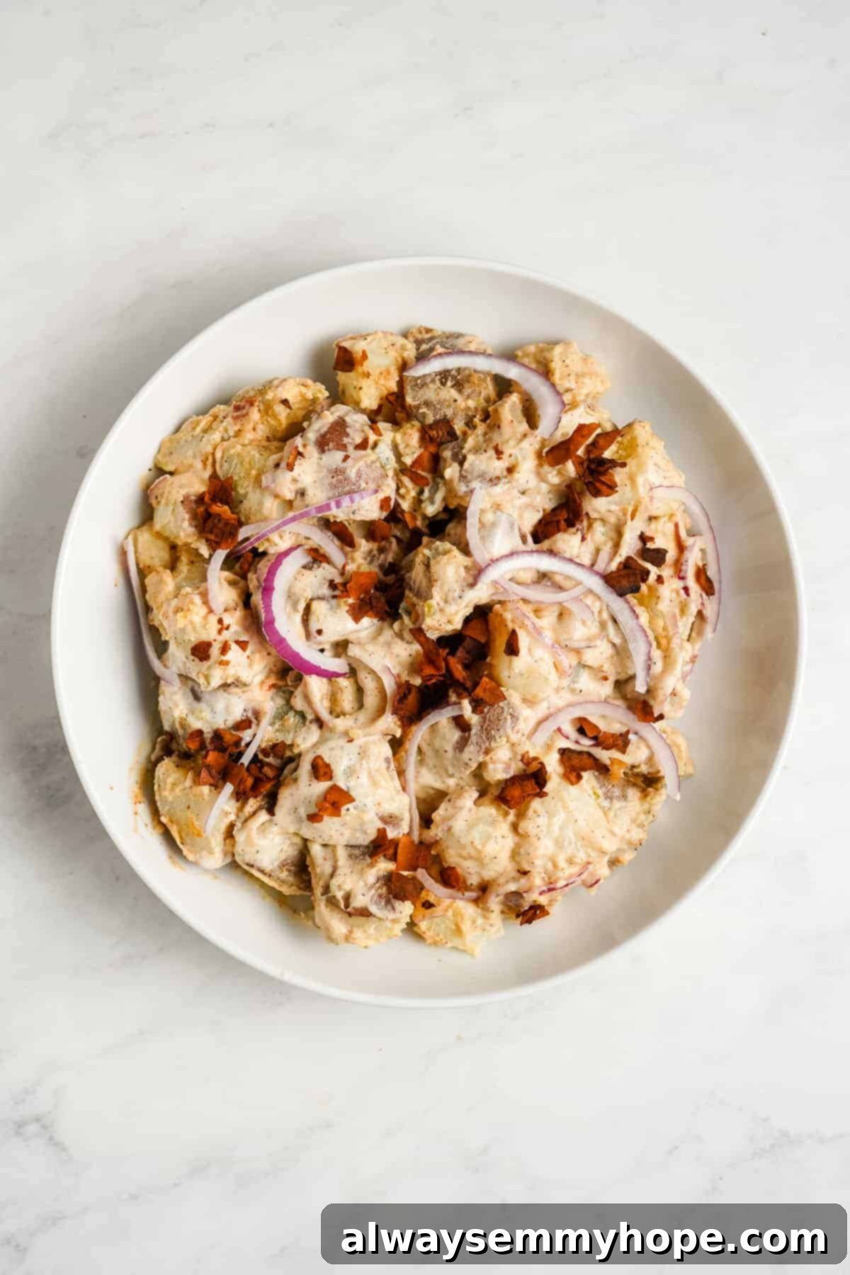 A plate of creamy vegan potato salad garnished with fresh herbs and a sprinkle of paprika.