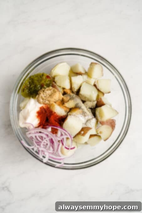 Mixing bowl with cooked potatoes, diced onion, spices, and condiments.