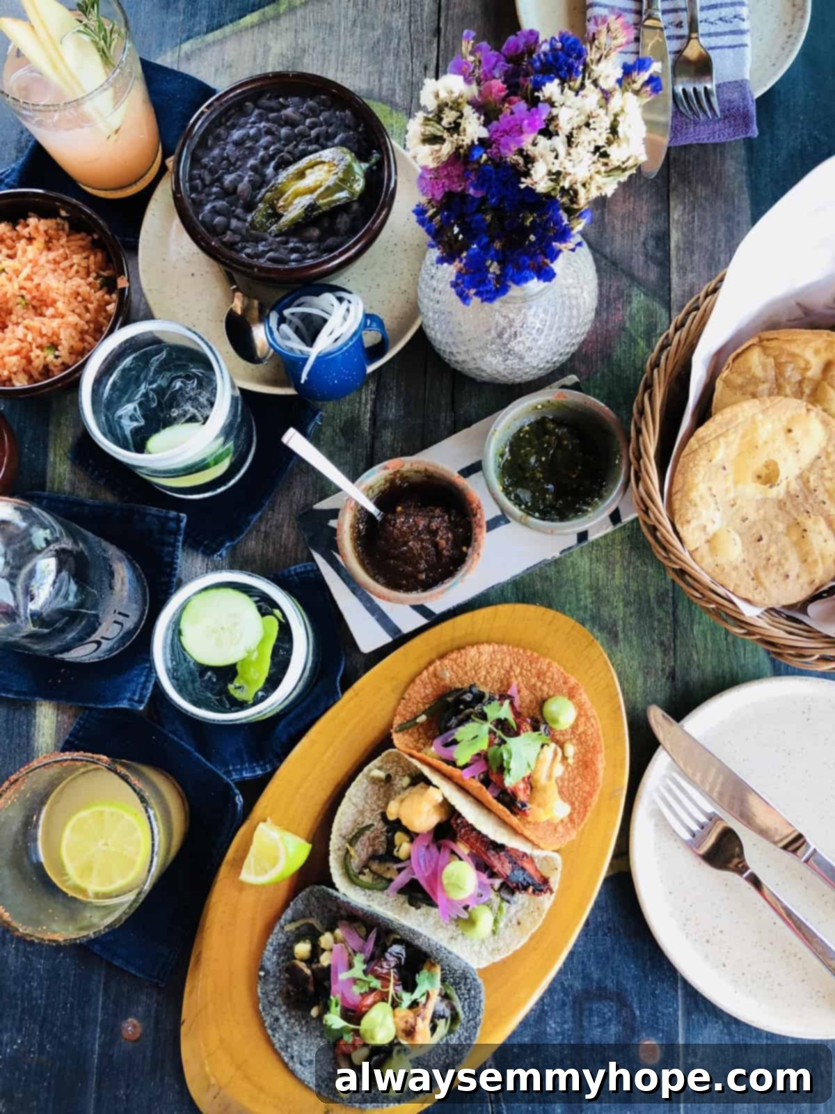 Top down view of an assortment of vibrant drinks, an array of sauces, and delicious tacos arranged on a wooden table.