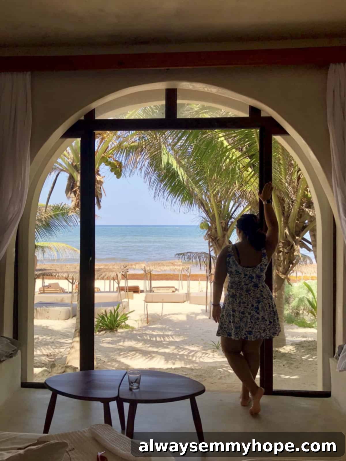 Jessica looking out from a luxurious hotel room balcony onto a pristine beach and turquoise ocean.