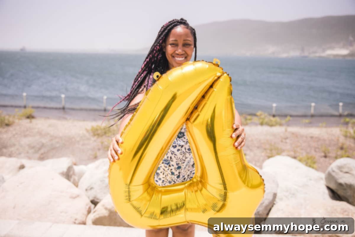Jessica smiling broadly while holding a large gold number four balloon on a sunny beach, celebrating her blog's anniversary.