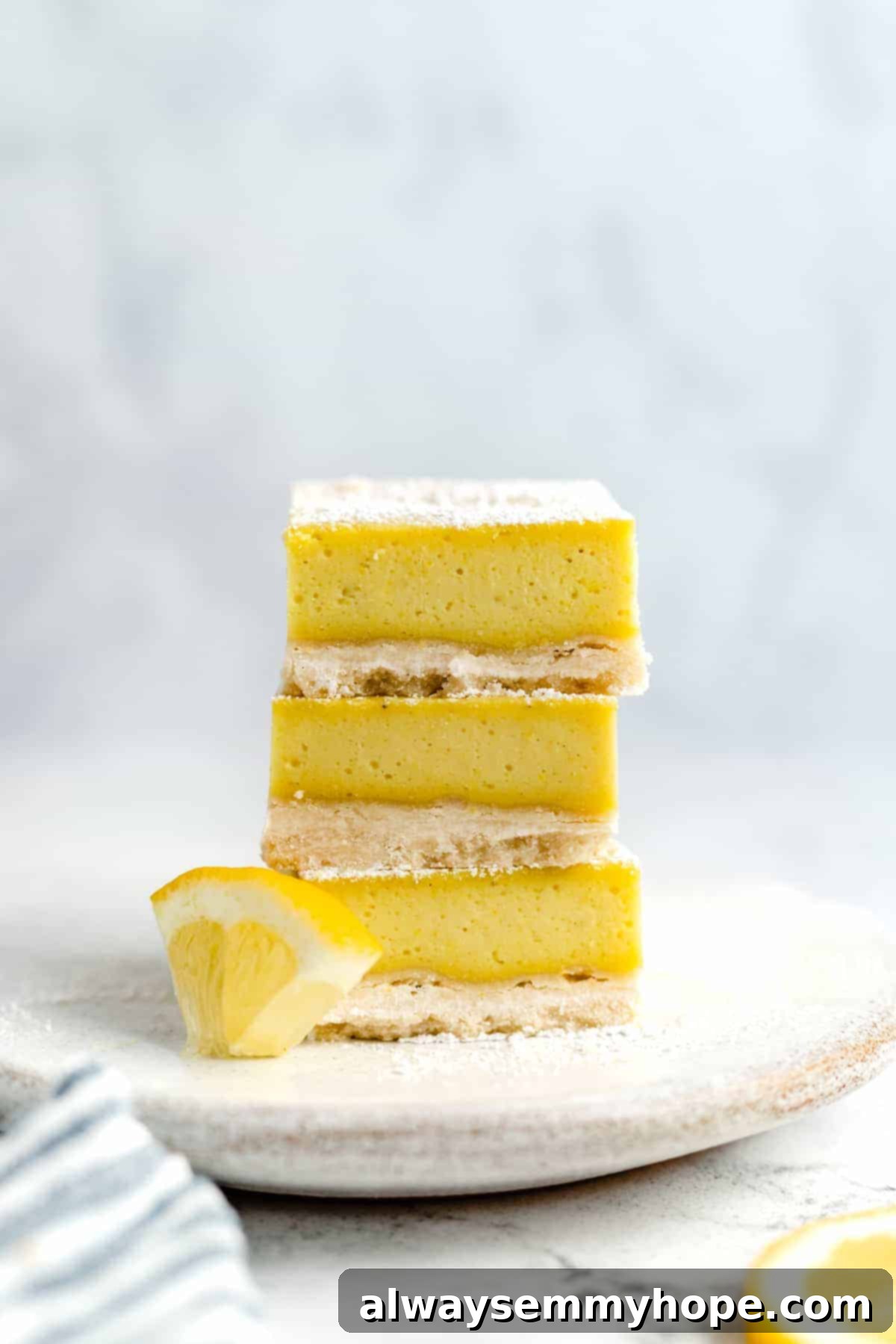 A stack of three perfectly cut vegan lemon bars, showcasing their layers and inviting texture.