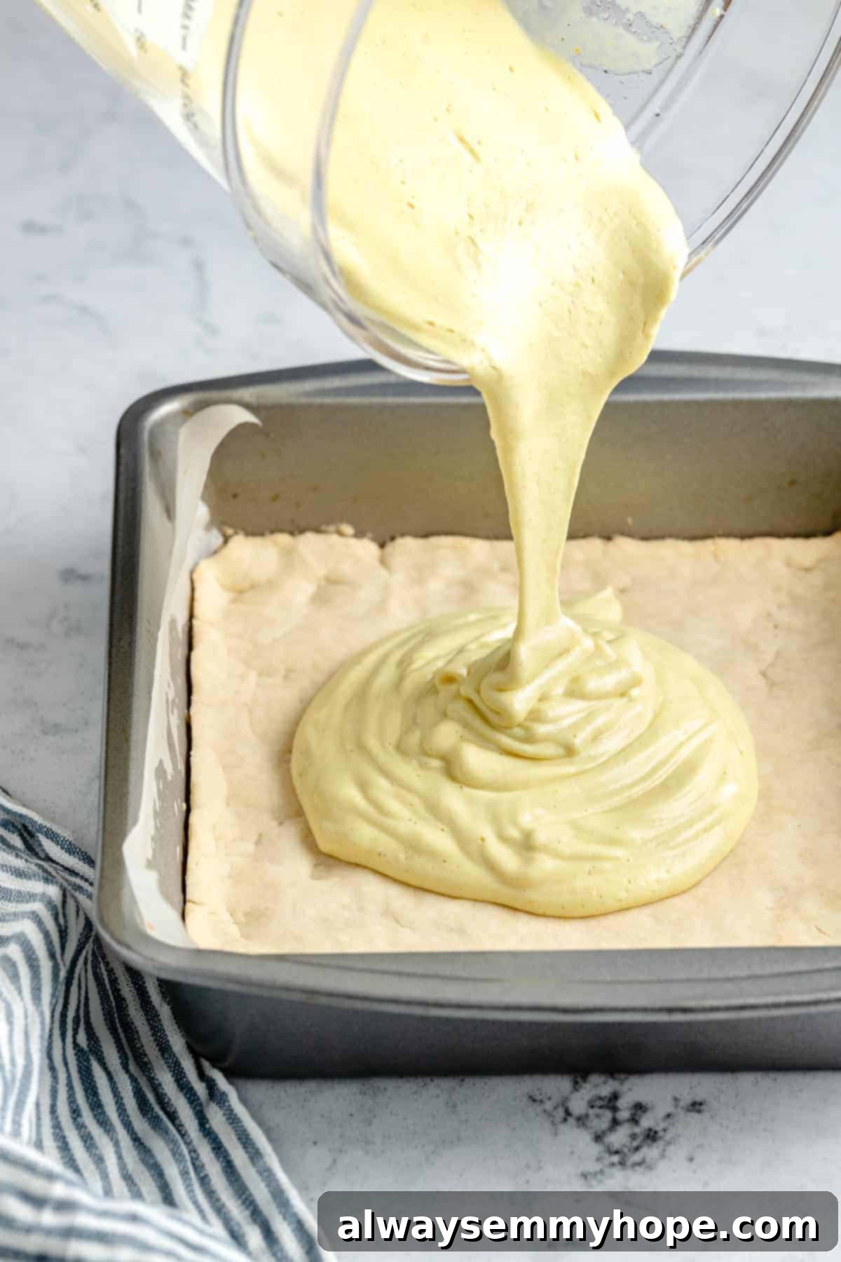 Smooth lemon filling being poured over a cooled shortbread crust in a baking pan.