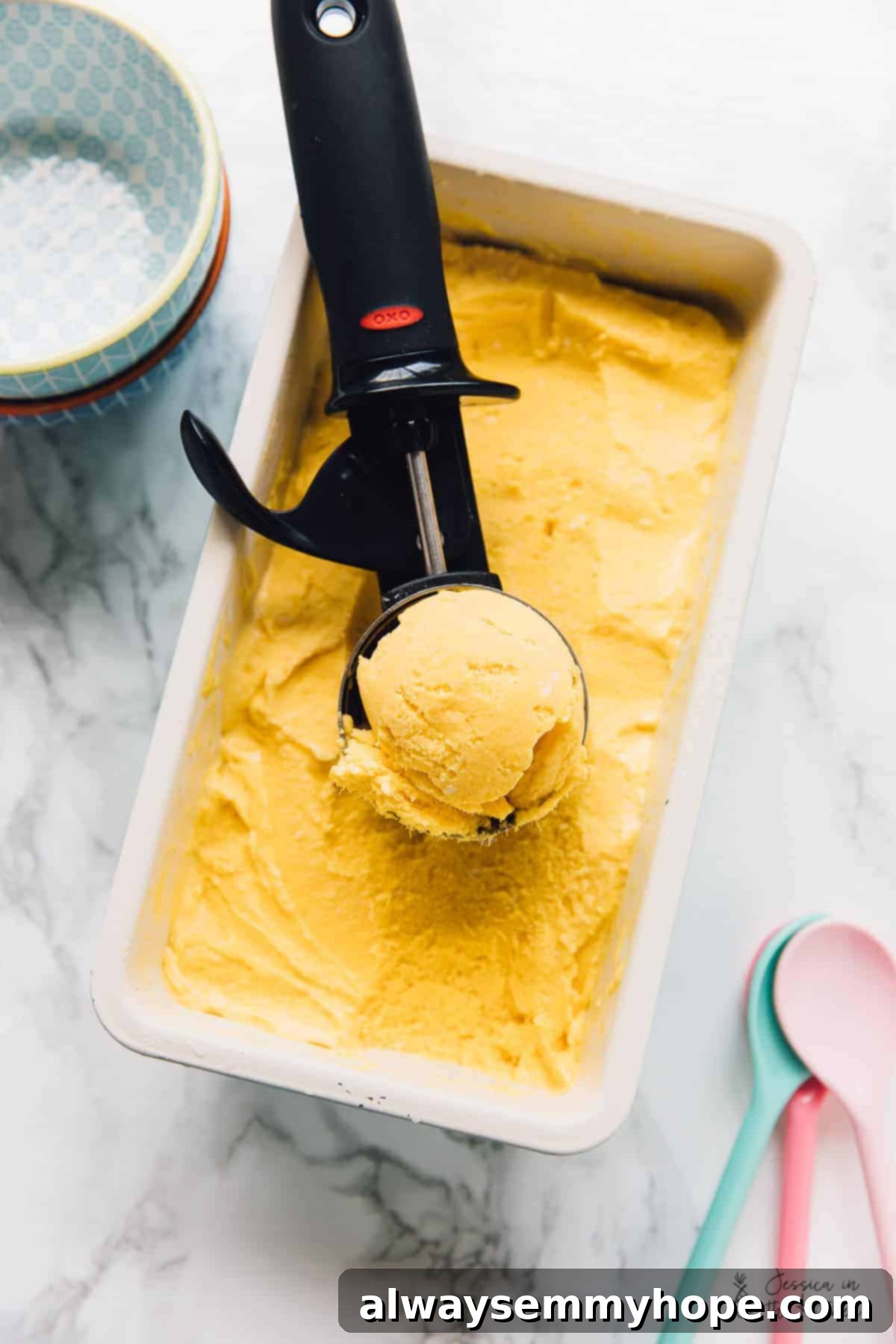 Vegan mango ice cream in an ice cream scoop resting on container of ice cream