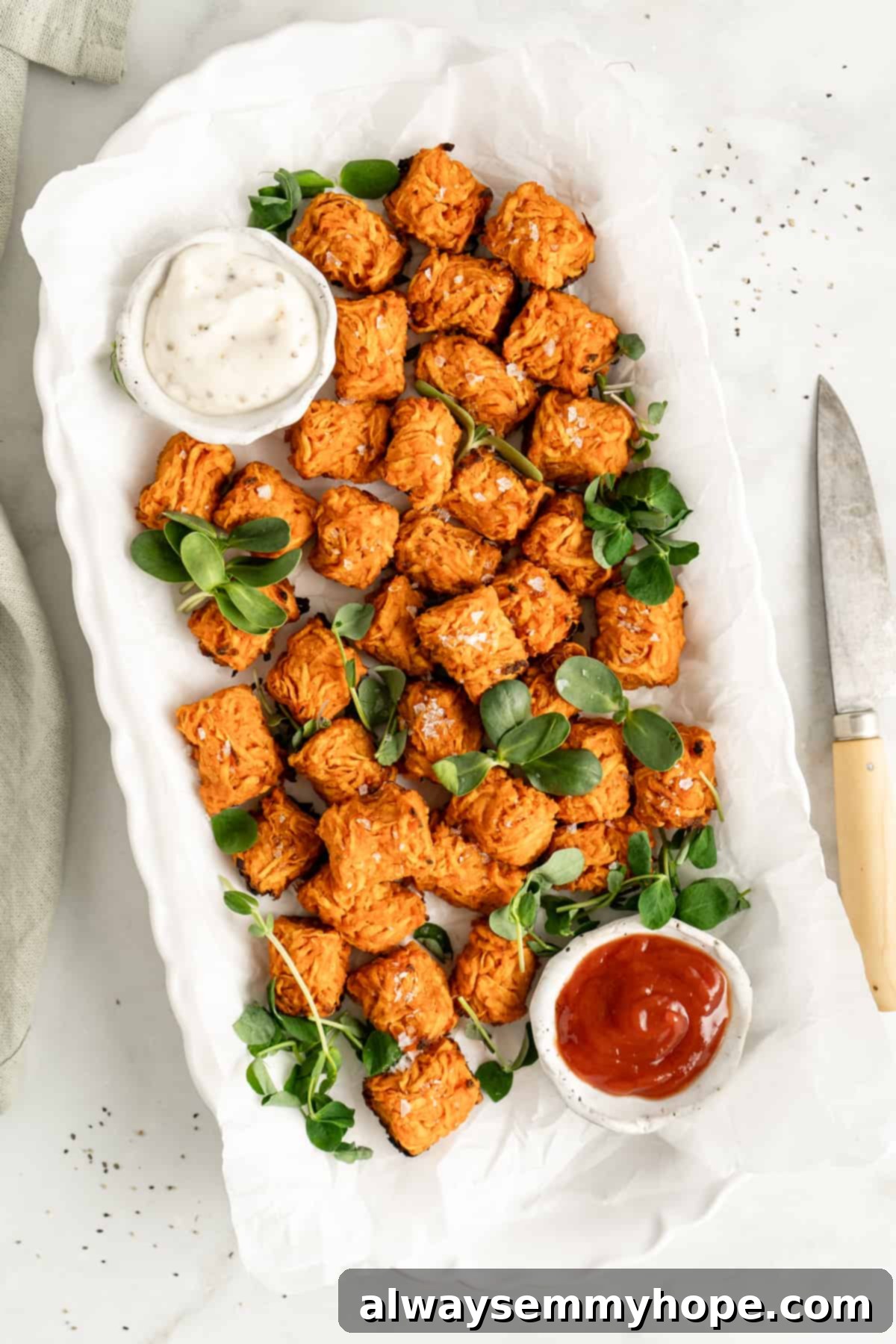 Overhead view of crispy sweet potato tots on a white platter with various dipping sauces in small bowls