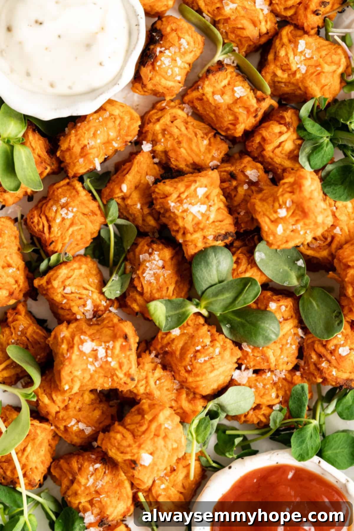 Overhead view of a serving platter filled with golden, crispy sweet potato tater tots and various dipping sauces