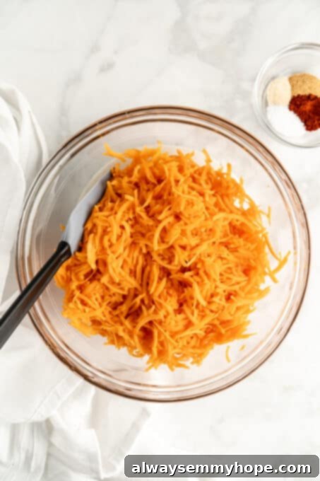 Glass bowl filled with freshly shredded sweet potatoes, with small bowl of seasonings in the background