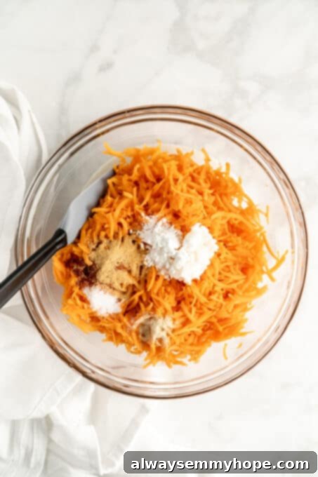 Shredded sweet potato and other tater tot ingredients (spices, cornstarch, oil) in a glass bowl, ready to be mixed