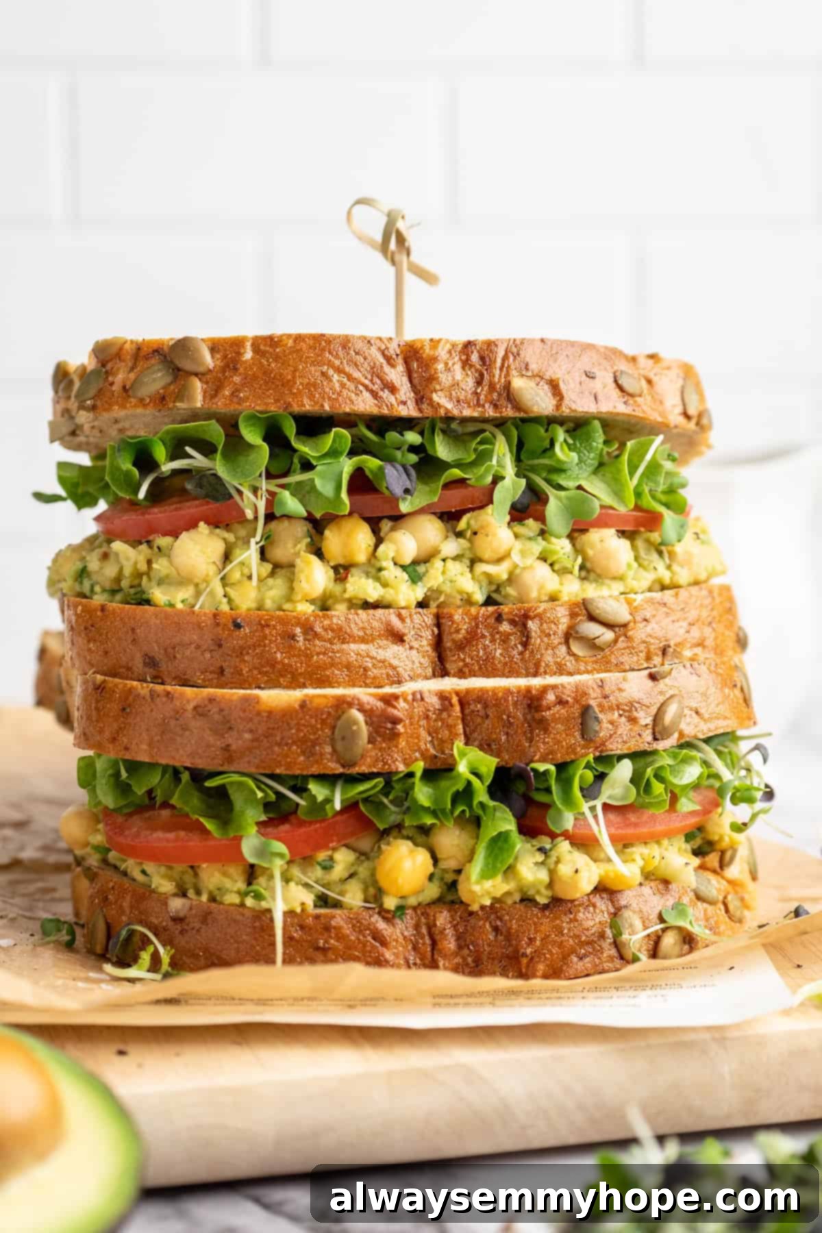 Two smashed chickpea avocado salad sandwiches stacked on cutting board, highlighting fresh ingredients and a vibrant green filling.