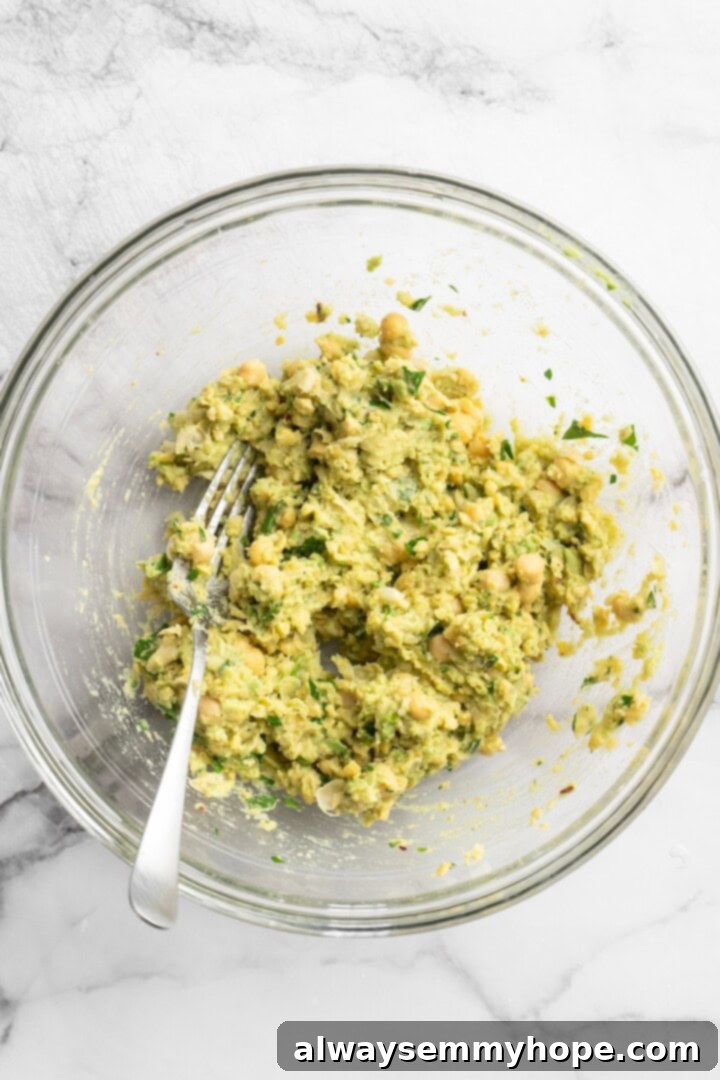 A bowl filled with freshly made smashed chickpea avocado salad, showing its creamy texture and green color, with a fork resting inside.
