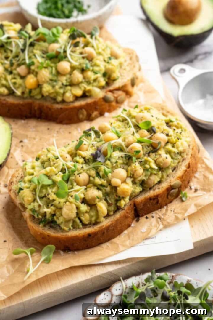 Two slices of bread topped generously with smashed chickpea avocado salad and fresh microgreens, ready for assembly into a sandwich.