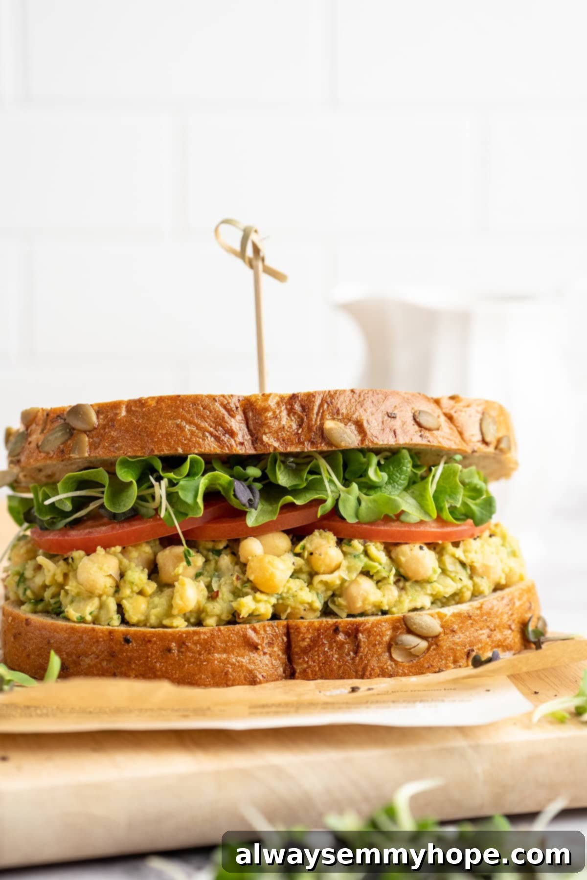 A beautifully assembled smashed chickpea avocado sandwich, with vibrant green filling and fresh toppings, ready to eat on a cutting board.