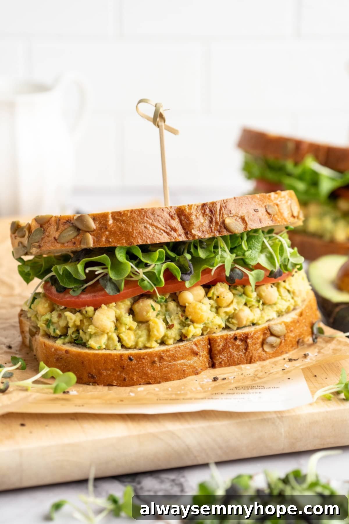 Close-up of a delicious smashed chickpea avocado salad sandwich, showcasing a thick filling with visible chickpeas, crisp lettuce, and a slice of red tomato.
