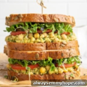 Two smashed chickpea avocado salad sandwiches stacked on cutting board