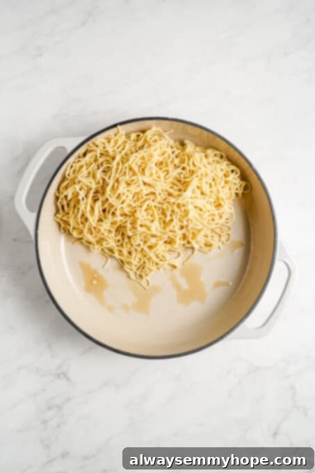 Noodles being stir-fried in a large pan with sesame oil.