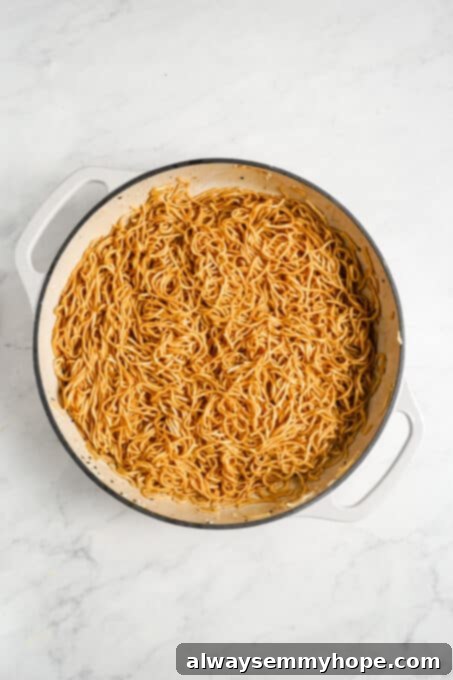 Noodles being thoroughly tossed in the maple ginger sauce in a pan.