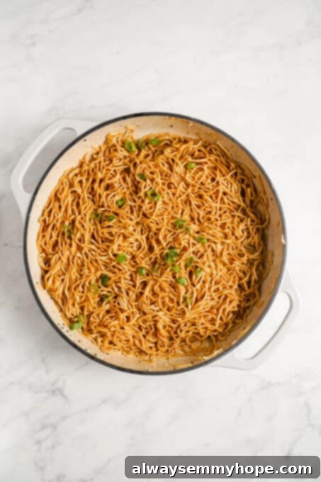 Finished sesame noodles in a pot, garnished with fresh green onions and sesame seeds.