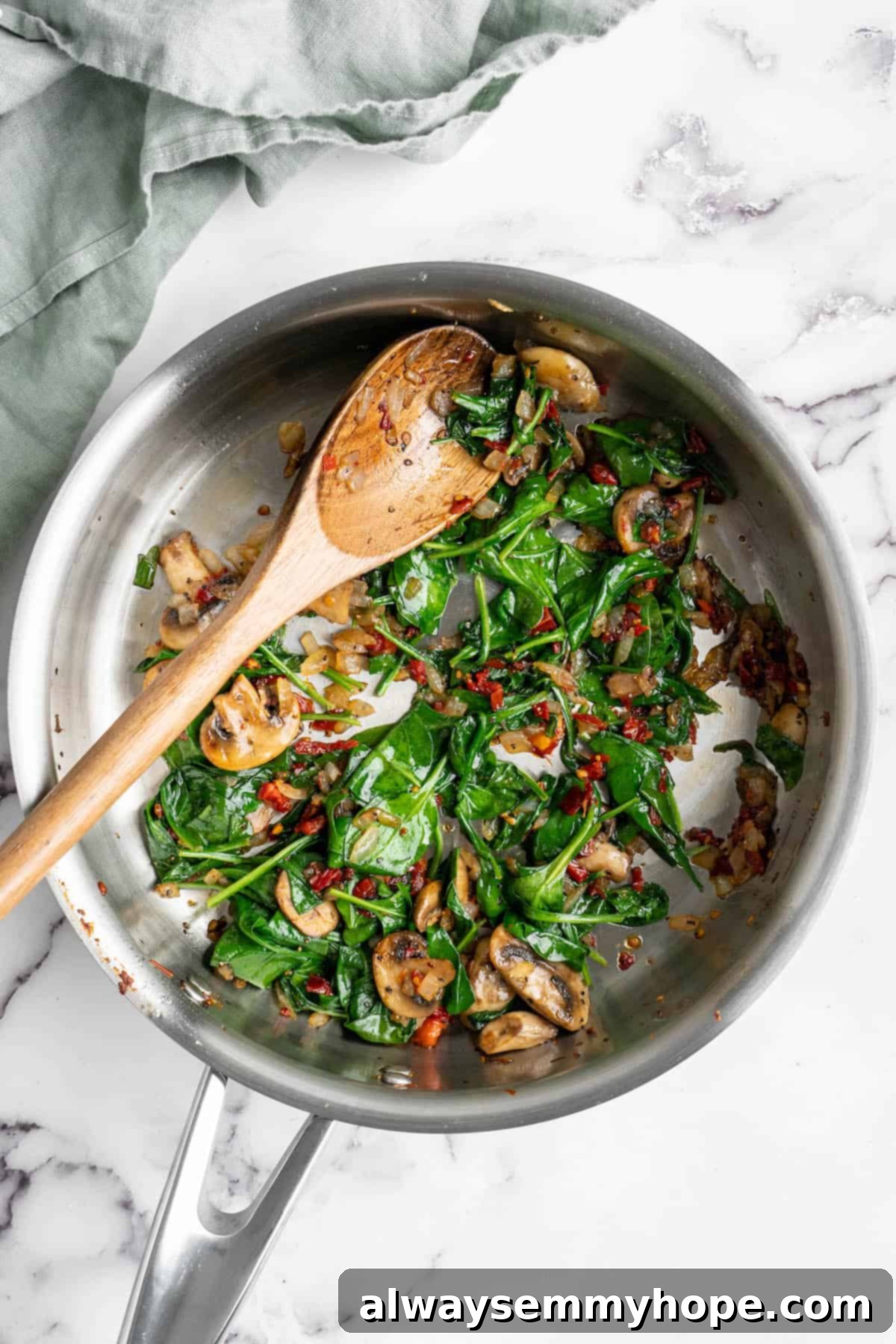Sautéed mushrooms, spinach, garlic, and onions simmering in a skillet with a wooden spoon.