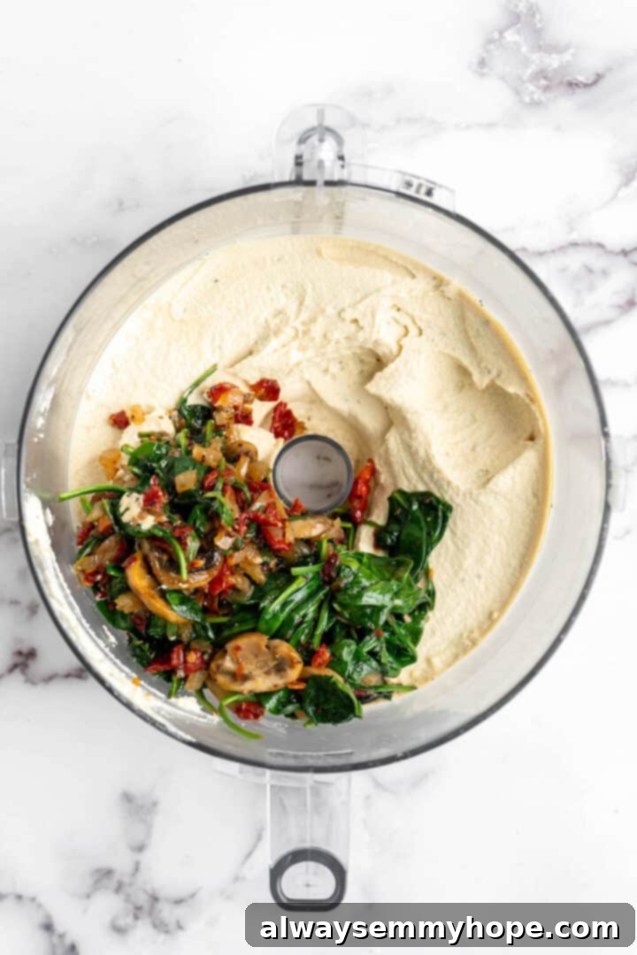 Sautéed vegetables being added to the smooth tofu quiche filling in a food processor bowl.
