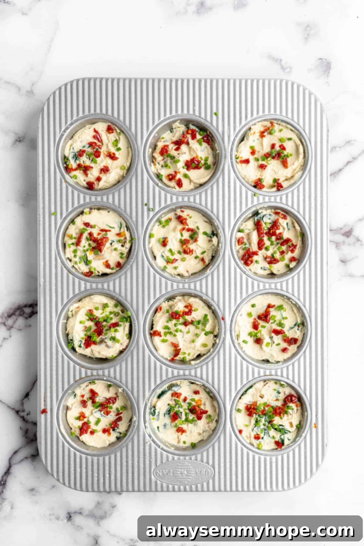 Unbaked vegan quiche muffins filled in a greased muffin tin, topped with sun-dried tomatoes.