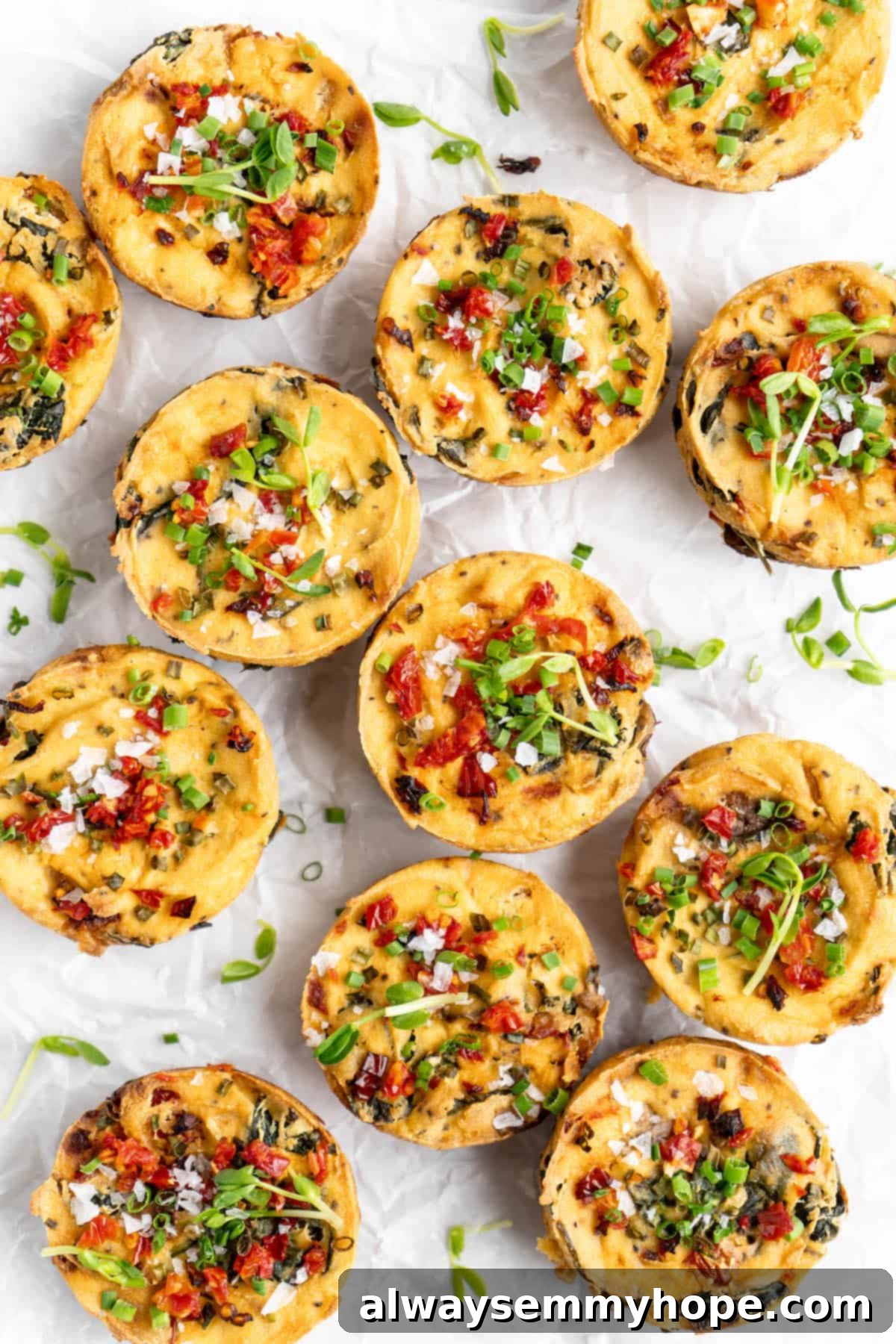 Arrangement of vegan quiche muffins on parchment paper, garnished with fresh herbs and sun-dried tomatoes.