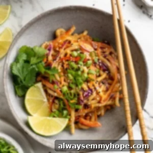 Overhead view of Thai peanut noodles in bowl with lime wedges, cilantro, and green onions for garnish