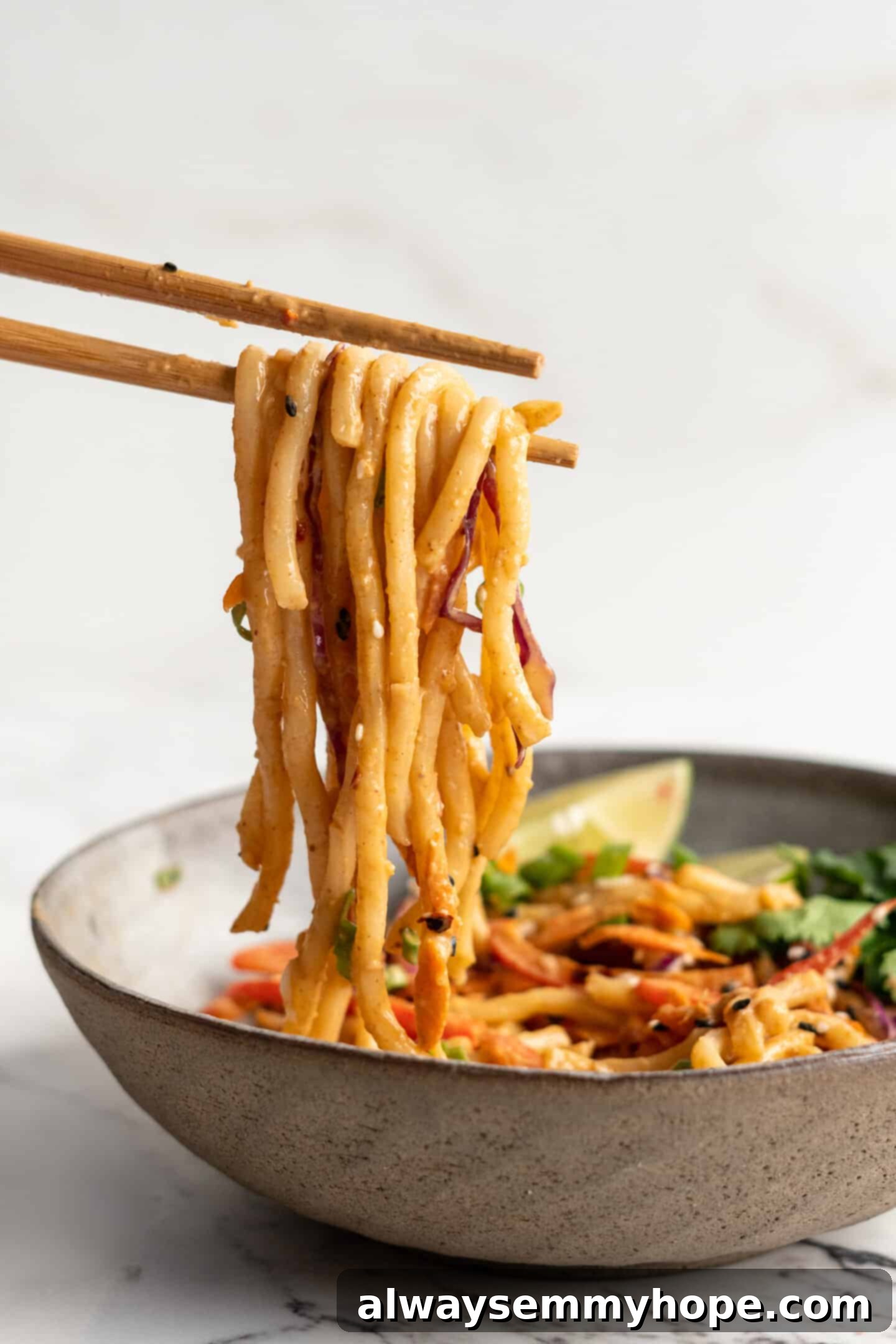 Thai peanut noodles being held with chopsticks above bowl