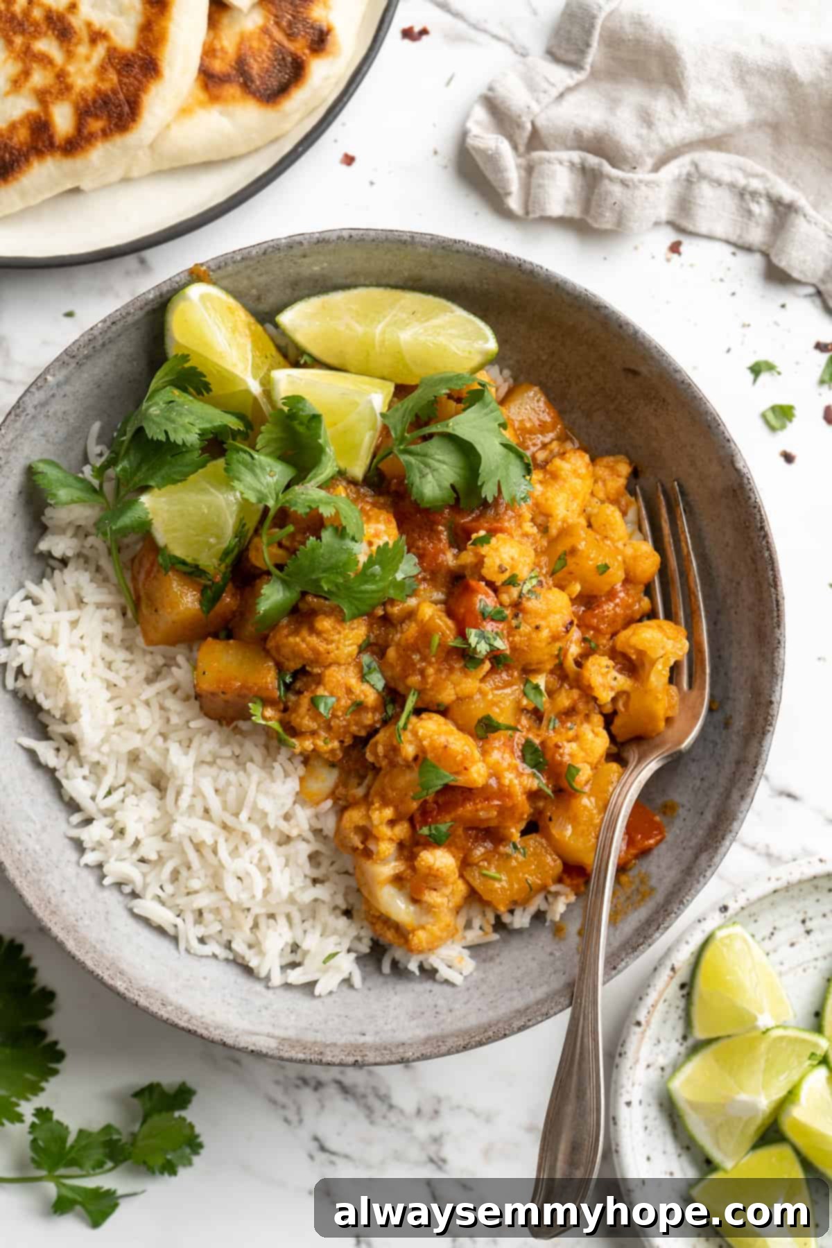 A vibrant bowl of Aloo Gobi, an Indian cauliflower and potato curry, garnished with fresh cilantro and a lime wedge, served alongside fluffy rice. Perfect for a hearty vegan meal.