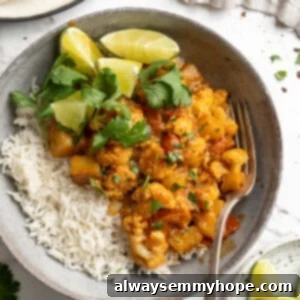 Overhead view of aloo gobi in bowl with rice, lime wedges, and cilantro