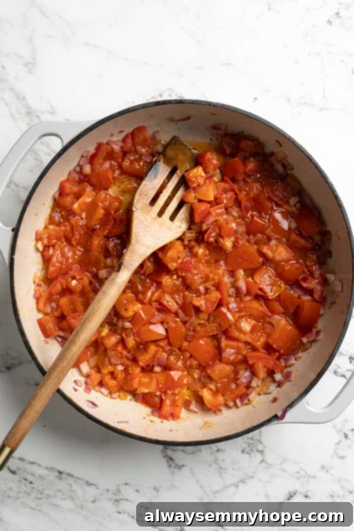 Chopped red onions and tomatoes sautéing in a pan with coconut oil, gently softening and releasing their juices.