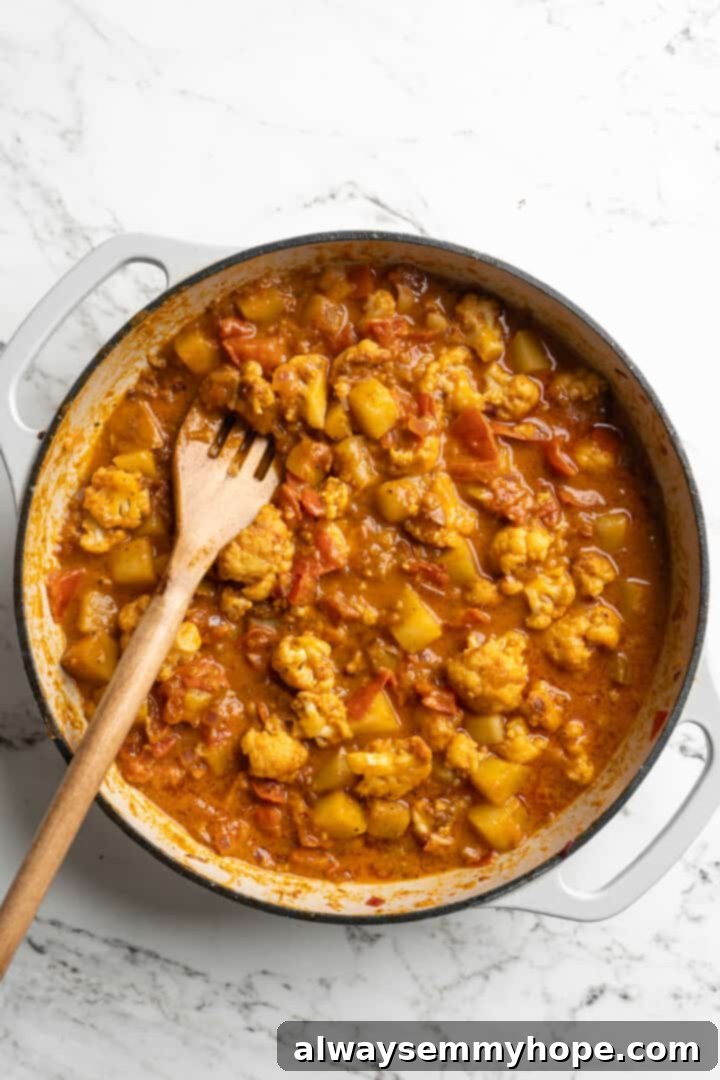 Aloo Gobi simmering in a pot, the cauliflower and potatoes fully coated in the creamy, spiced curry sauce, nearly ready to serve.