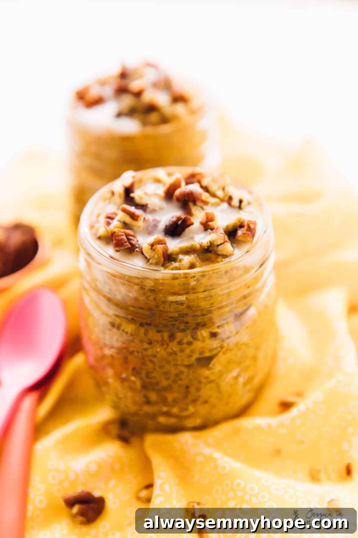 Easy vegan pumpkin chia pudding is rich, creamy, and full of fall flavors like hearty pumpkin, warm spices, and buttery pecans. A jar of chia pudding topped with pecans, with another jar and a spoon in the background