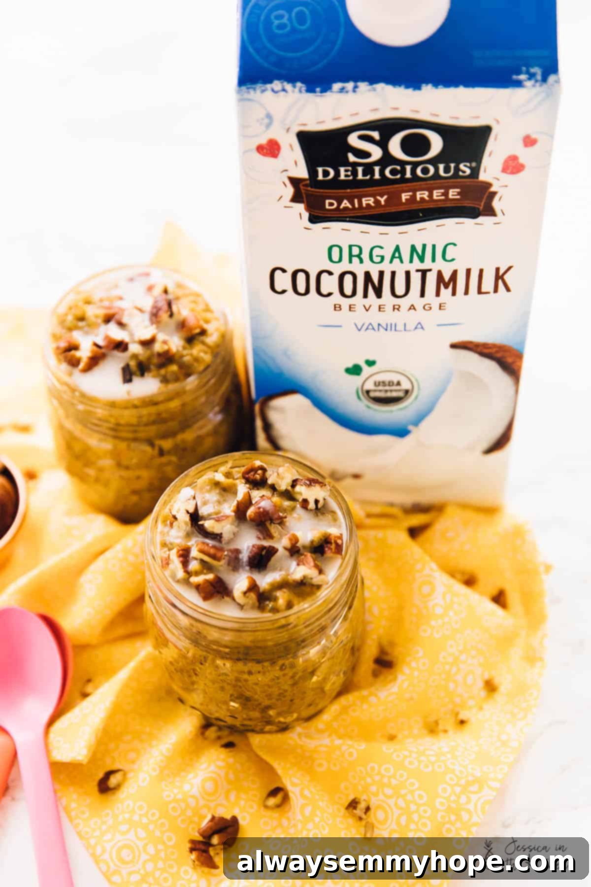 Easy vegan pumpkin chia pudding is rich, creamy, and full of fall flavors like hearty pumpkin, warm spices, and buttery pecans. Two jars of chia pudding topped with pecans, next to two spoons and a carton of coconut milk beverage.