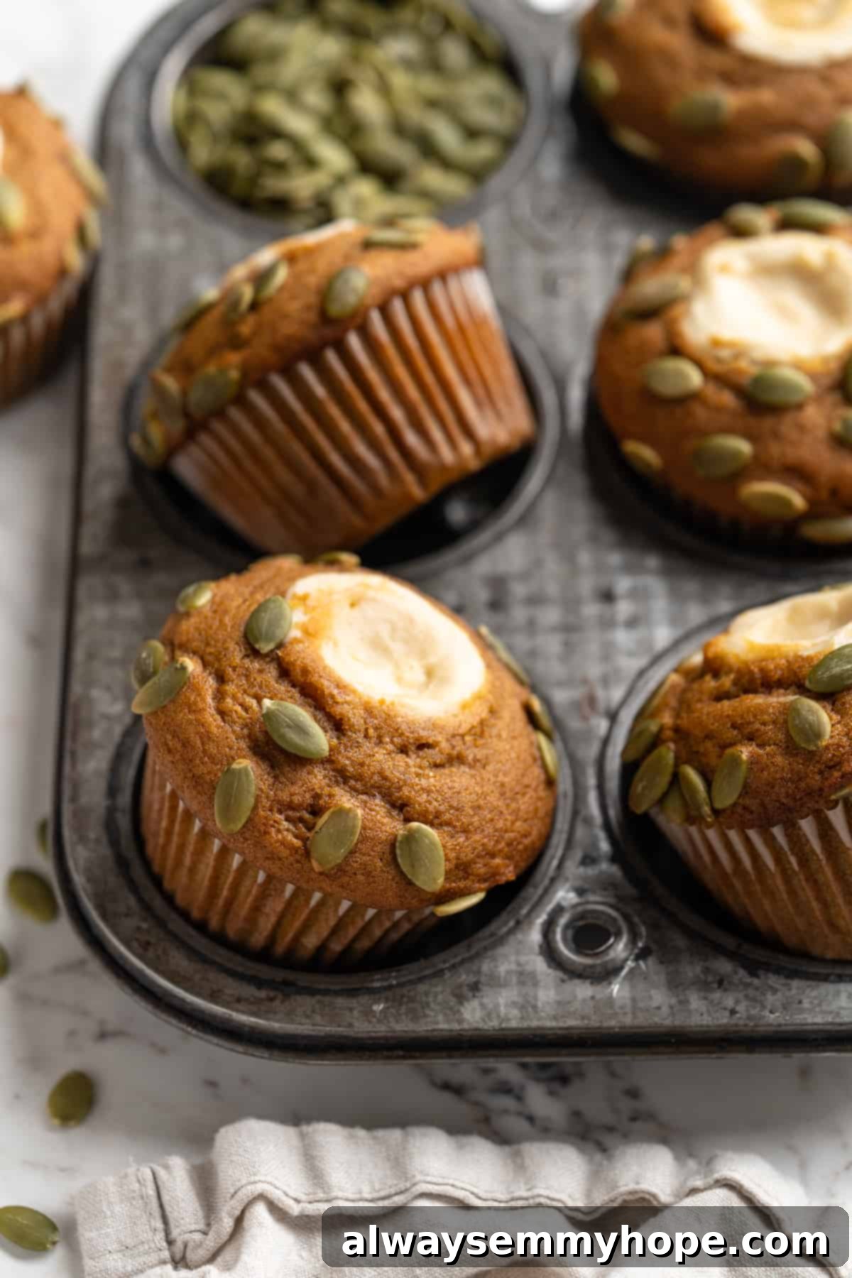 These vegan pumpkin cream cheese muffins pair the cozy flavour of pumpkin with a sweet-and-tangy cream cheese filling with delicious results! Pumpkin cream cheese muffins freshly baked in a muffin pan, showcasing their golden-brown tops and visible cream cheese swirl.