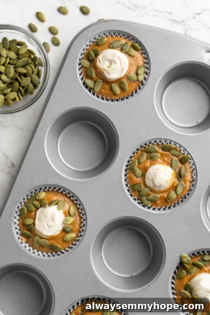 These vegan pumpkin cream cheese muffins pair the cozy flavour of pumpkin with a sweet-and-tangy cream cheese filling with delicious results! Overhead view of pumpkin cream cheese muffins in a pan, ready for baking with the filling swirled in.
